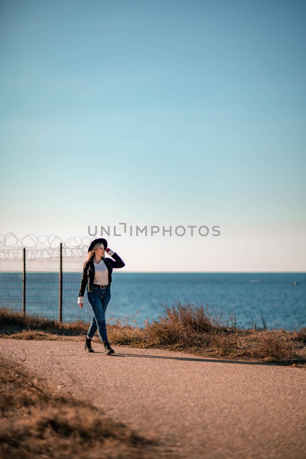 A blonde in a stylish black leather jacket walks along the seashore