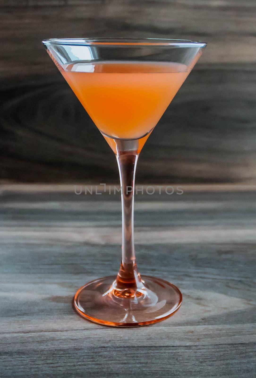 Martini glass of orange cocktail on a wooden table