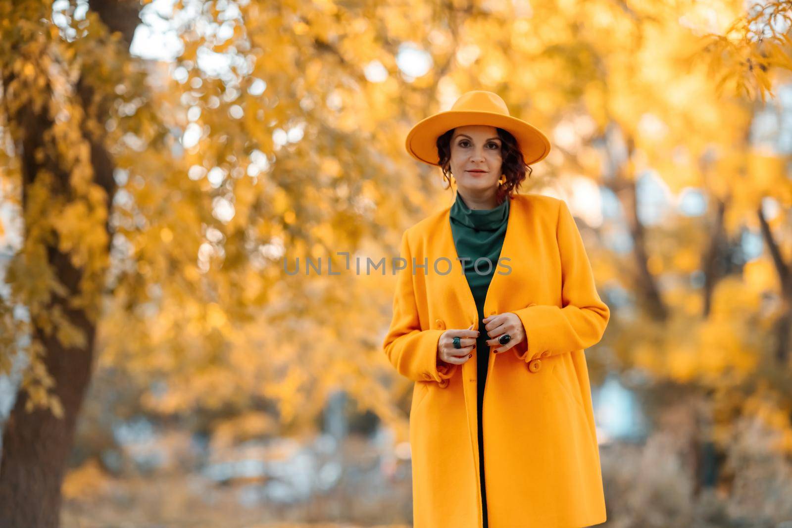 Beautiful woman walks outdoors in autumn. She is wearing a yellow coat, yellow hat and green dress. Young woman enjoying the autumn weather. Autumn content by Matiunina