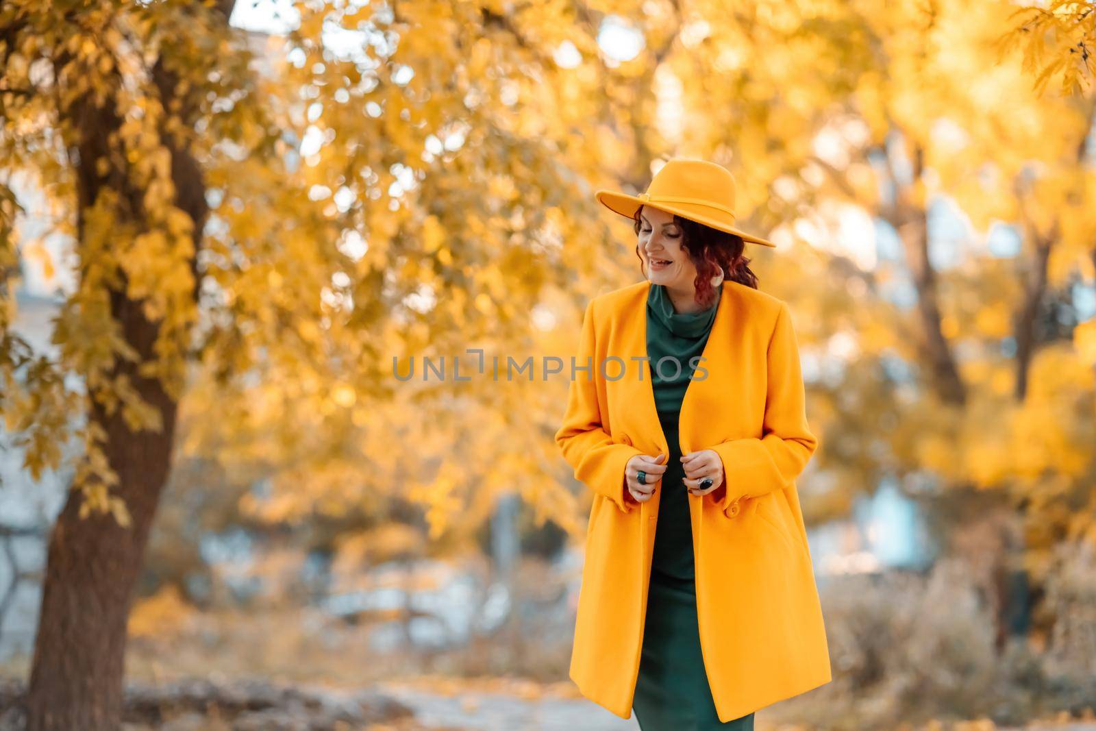 Beautiful woman walks outdoors in autumn. She is wearing a yellow coat, yellow hat and green dress. Young woman enjoying the autumn weather. Autumn content.