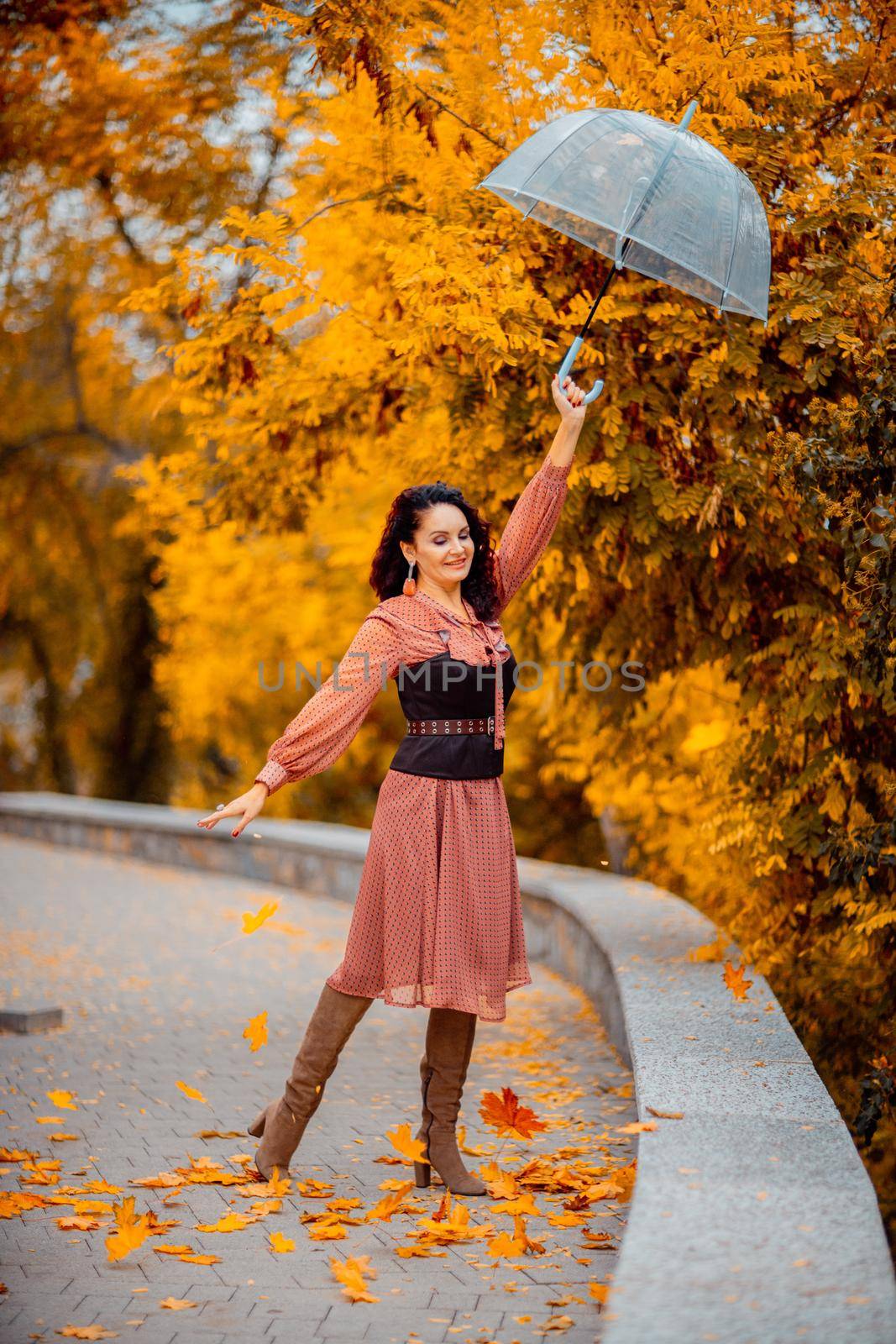 Beautiful girl in a dress with an umbrella in the autumn park. She holds him over her head, autumn leaves are falling out of him by Matiunina