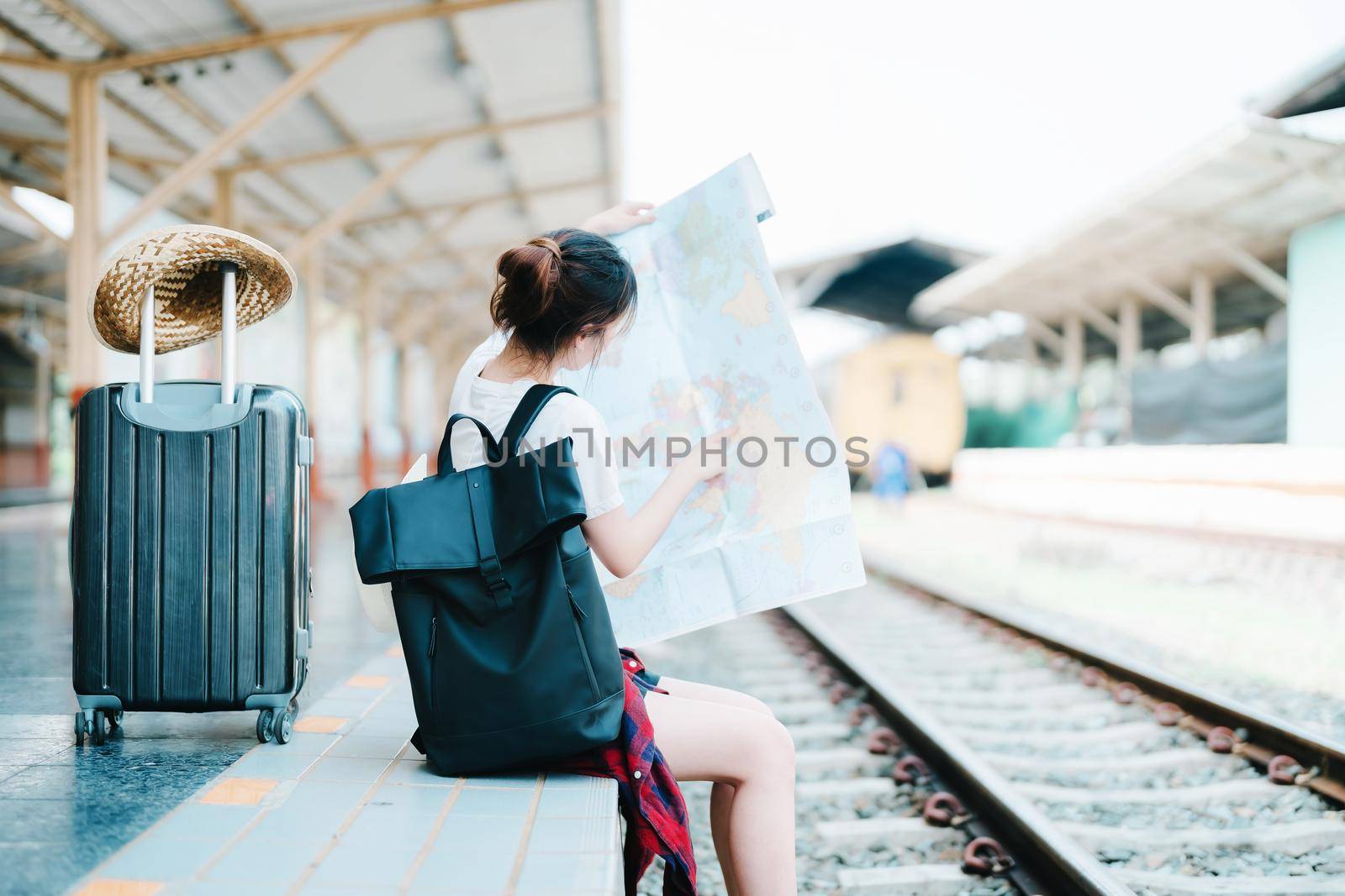 summer, relax, vacation, travel, portrait of a cute Asian girl looking at a map to plan a trip while waiting at the train station. by Manastrong