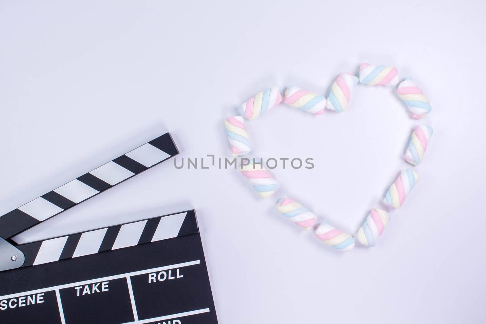 Movie clapperboard with heart shaped from twisted marshmallows. Valentine's day concept. Love. White background with twisted marshmallow pattern. Mock up. Space for text by JuliaDorian