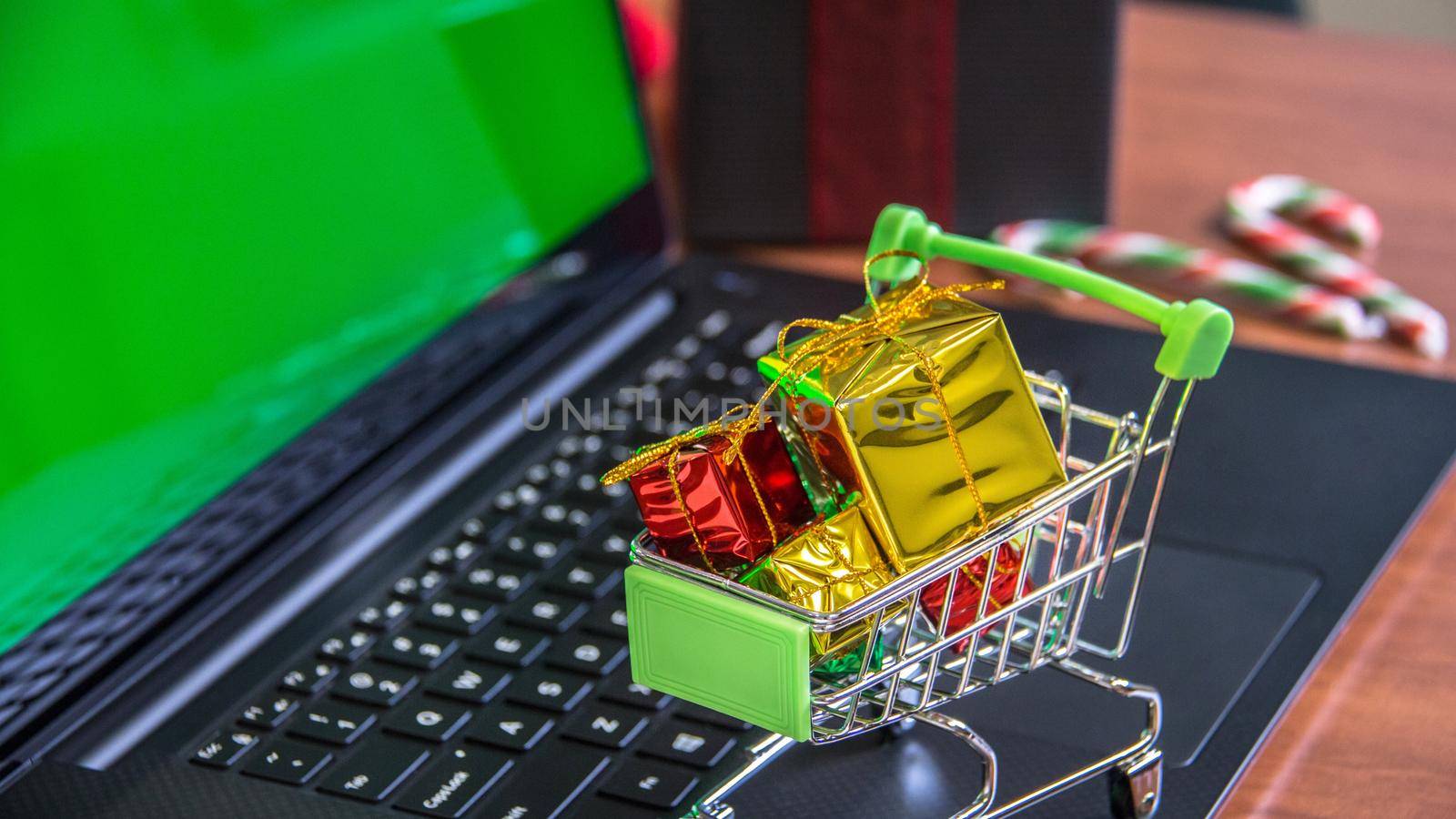 Shopping cart full of christmas gifts on laptop computer with green screen. Online shopping, e-commerce and worldwide shipping concept. Mockup, space for text.