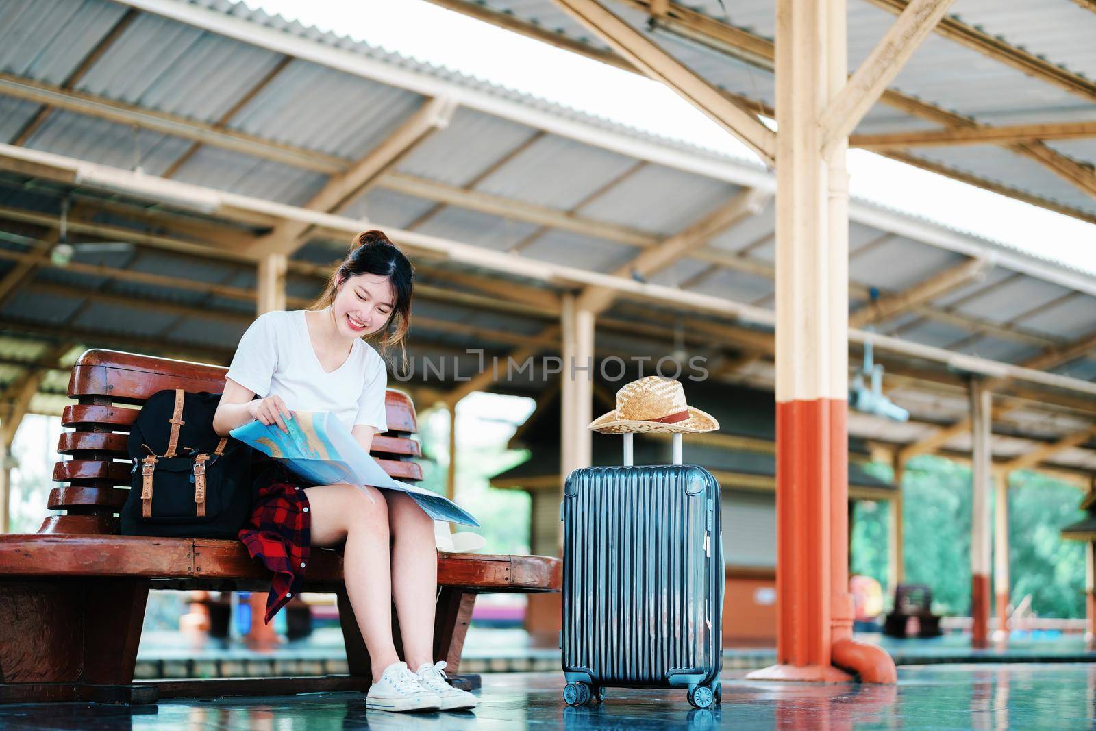 summer, relax, vacation, travel, portrait of a cute Asian girl looking at a map to plan a trip while waiting at the train station