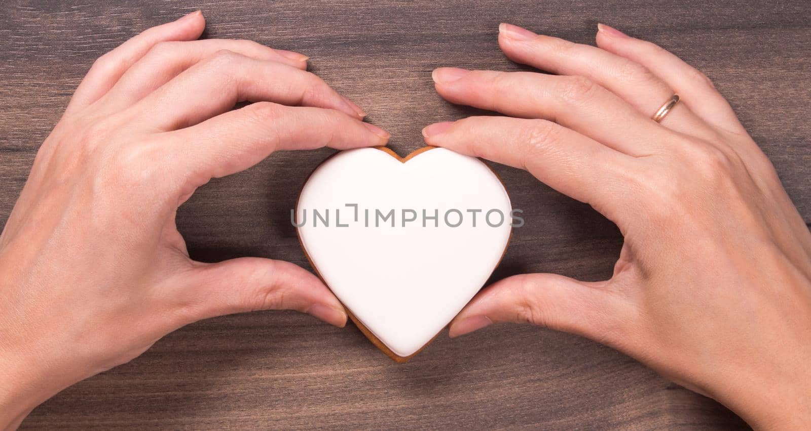 Two hands holding white heart shape cookie for Mothers day, Womans day or Valentines Day on wooden background. Copy space.