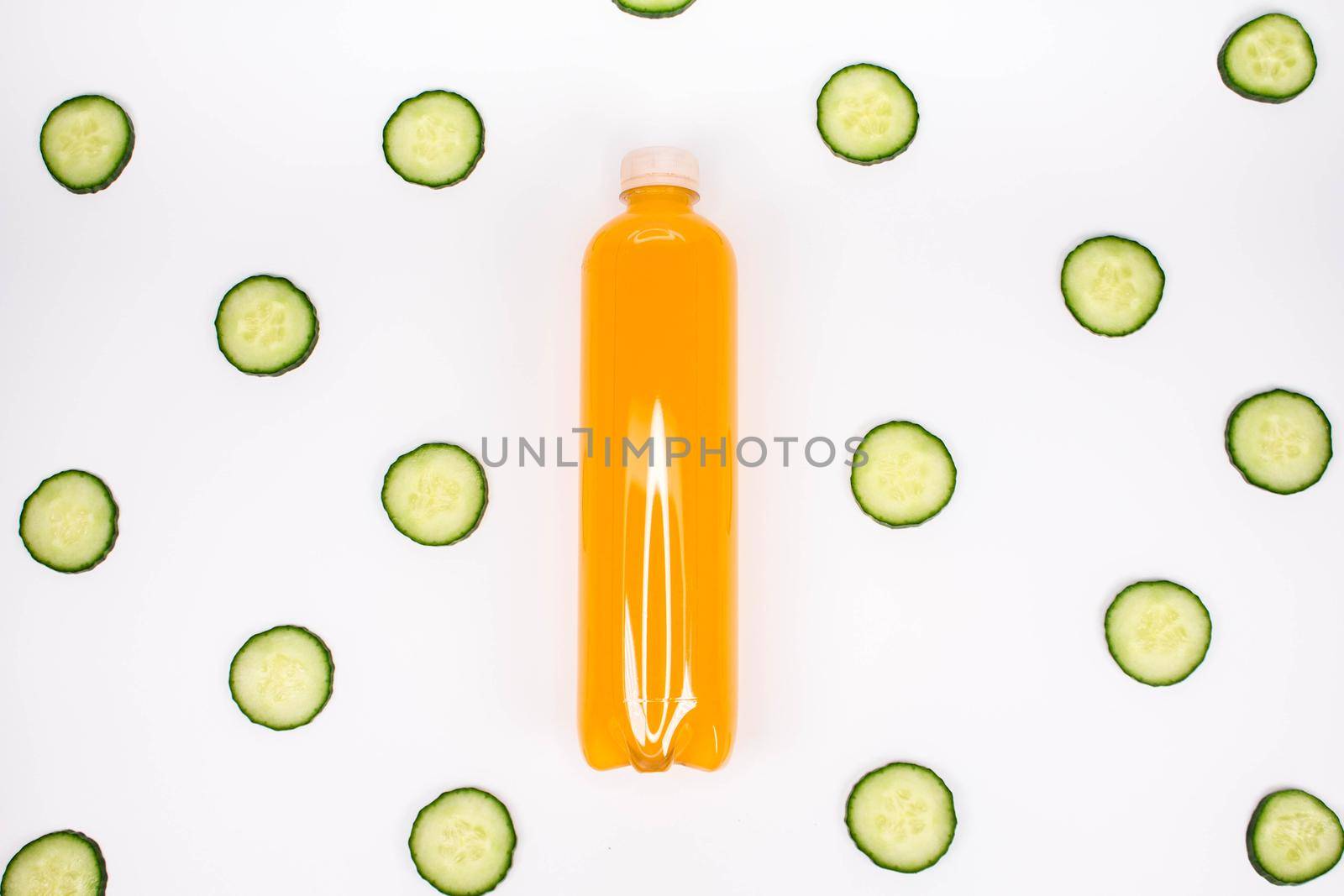 Bottle of orange smoothie on white background cucumber pattern. Top view. Detox summer drink. Healthy fresh juice bottle. Vegan and vegetarian concept.