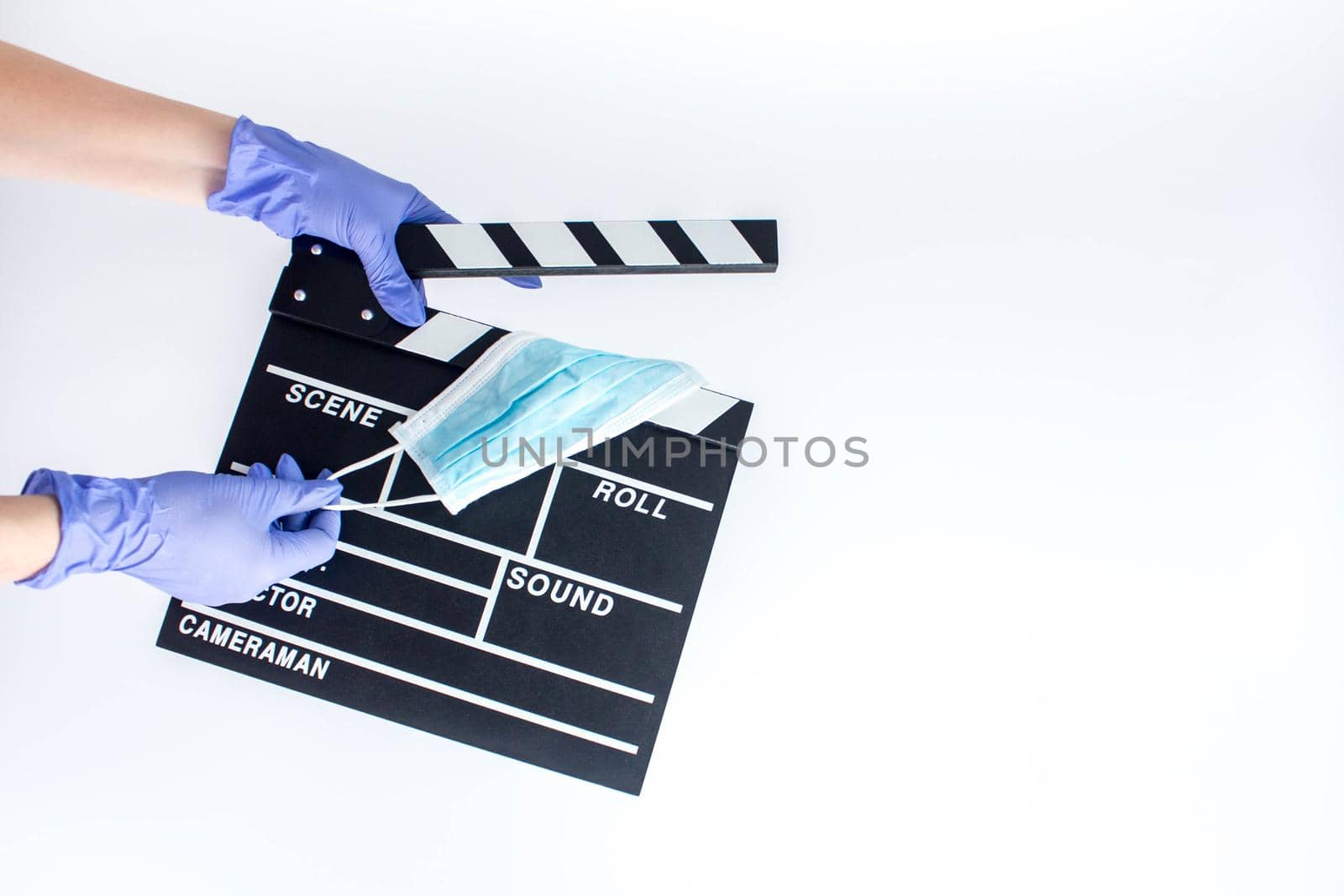 Hands in blue disposable rubber gloves holding openned movie clapper. Wants to remove medical mask. Influence of pandemic on cinematography by JuliaDorian