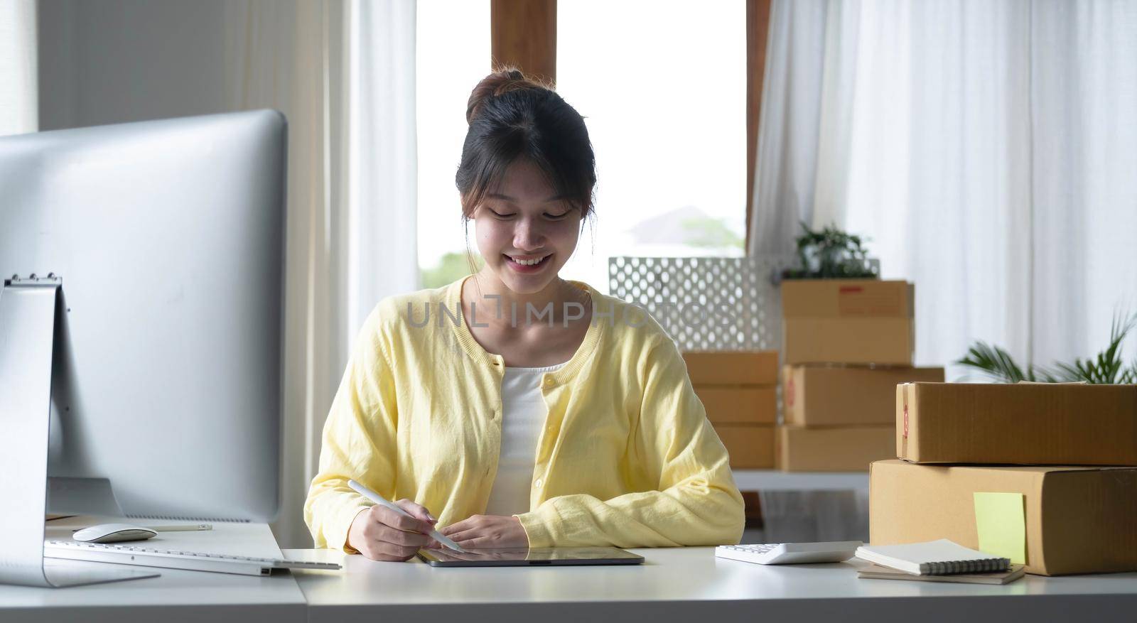 Portrait business Asian woman smile and use tablet checking information on parcel shipping box before send to customer. Entrepreneur small business working at home. SME business online marketing..