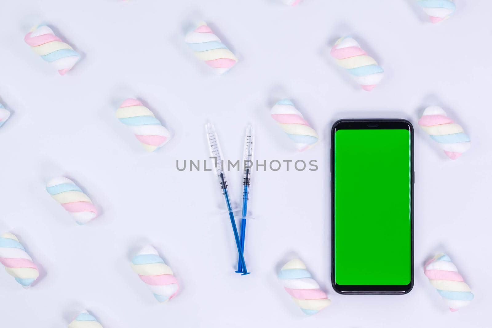 Phone mockup. Syringe with needle and black smartphone with blank screen. White background with twisted marshmallow pattern.