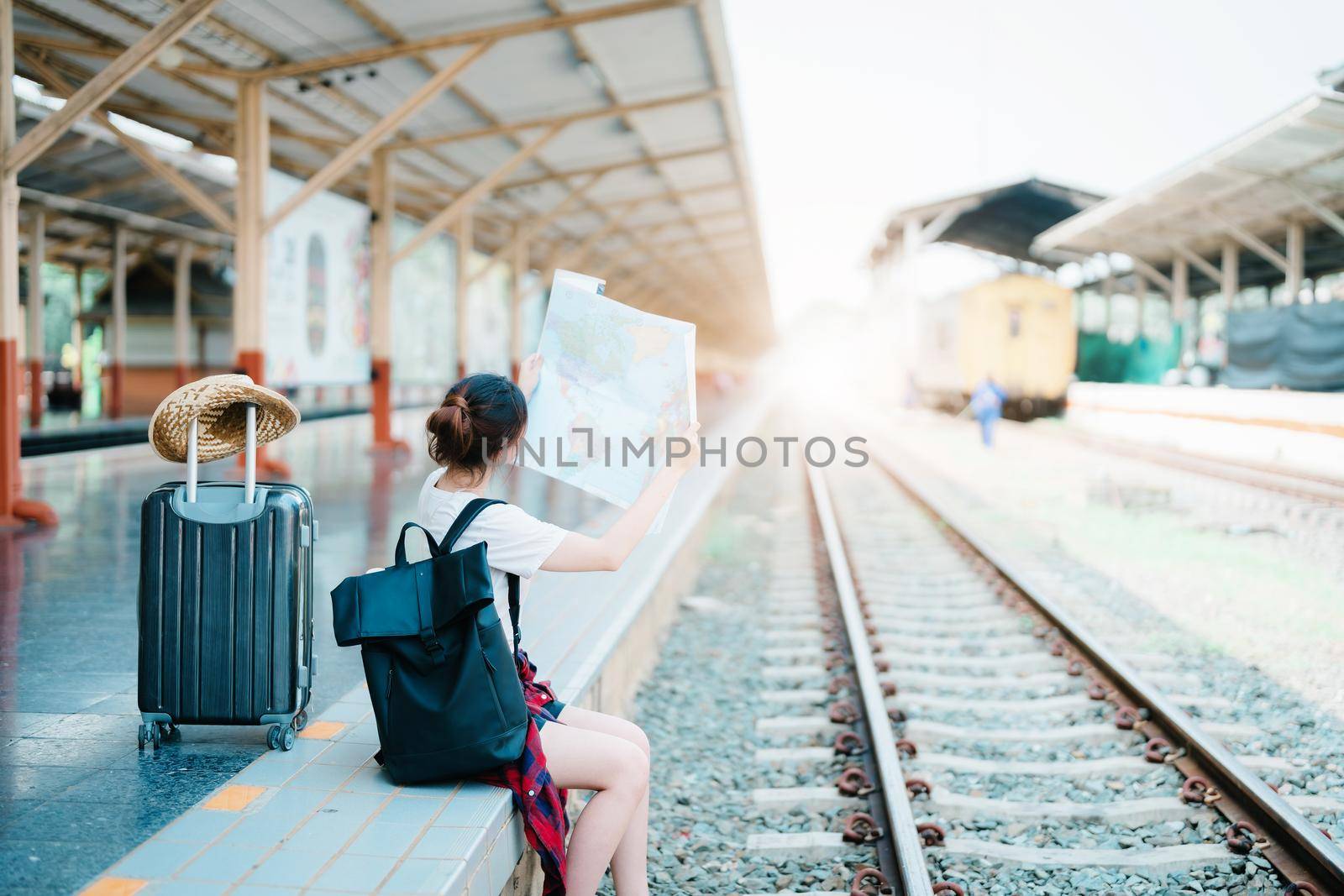 summer, relax, vacation, travel, portrait of a cute Asian girl looking at a map to plan a trip while waiting at the train station. by Manastrong