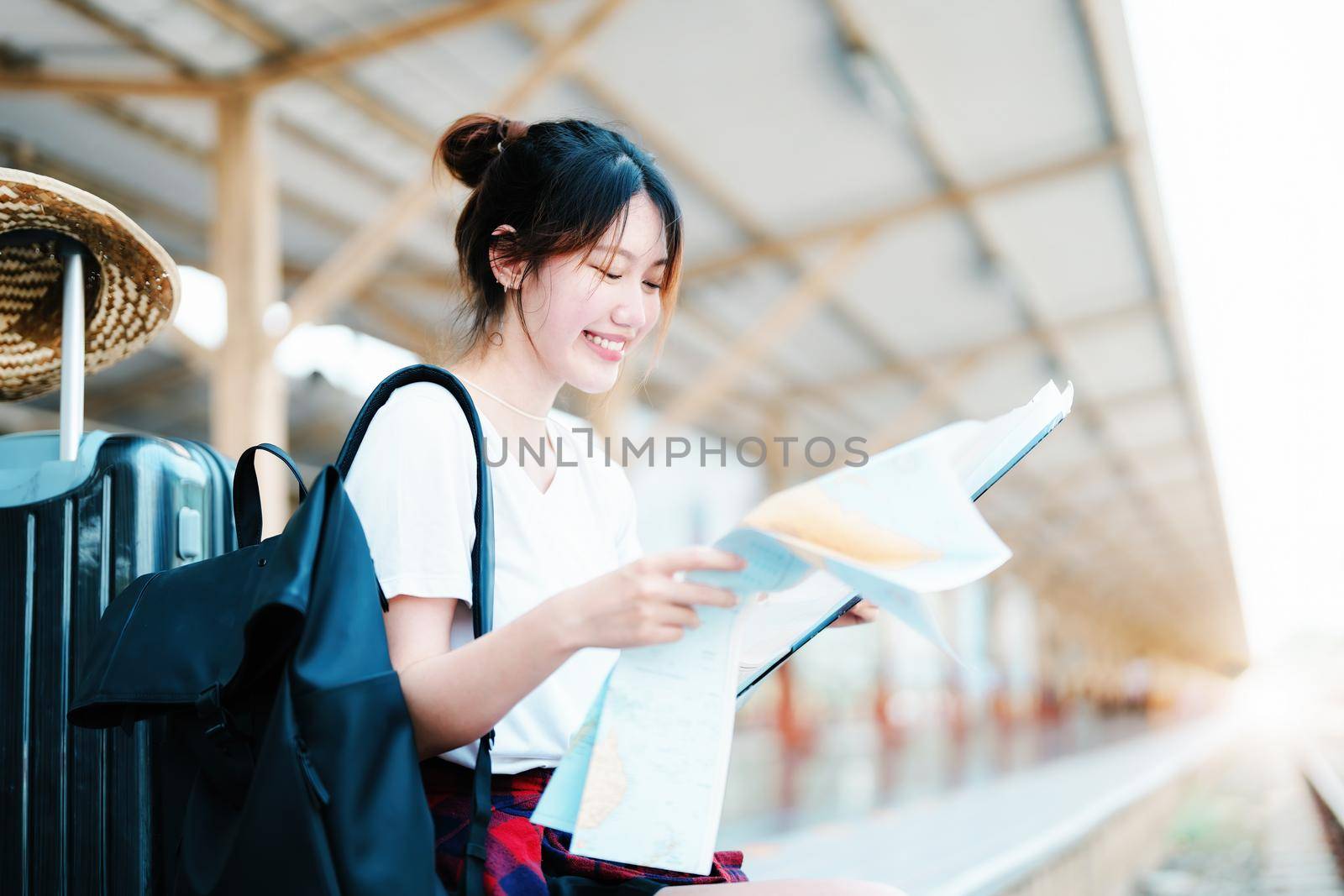 summer, relax, vacation, travel, portrait of a cute Asian girl looking at a map to plan a trip while waiting at the train station. by Manastrong