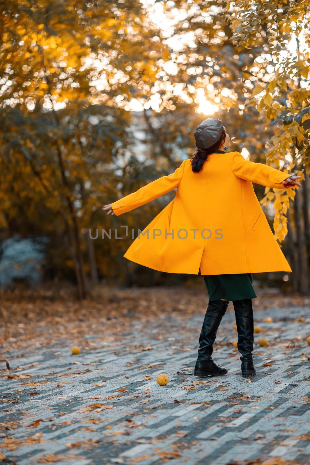 Beautiful woman walks outdoors in autumn. She is wearing a yellow coat and a green dress. Young woman enjoying the autumn weather. Autumn content. by Matiunina