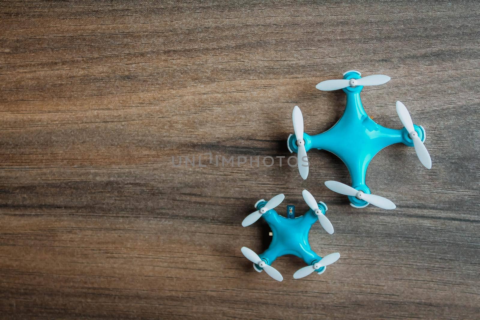 View of tiny drone on a wooden background. Small blue drone with white propellers.