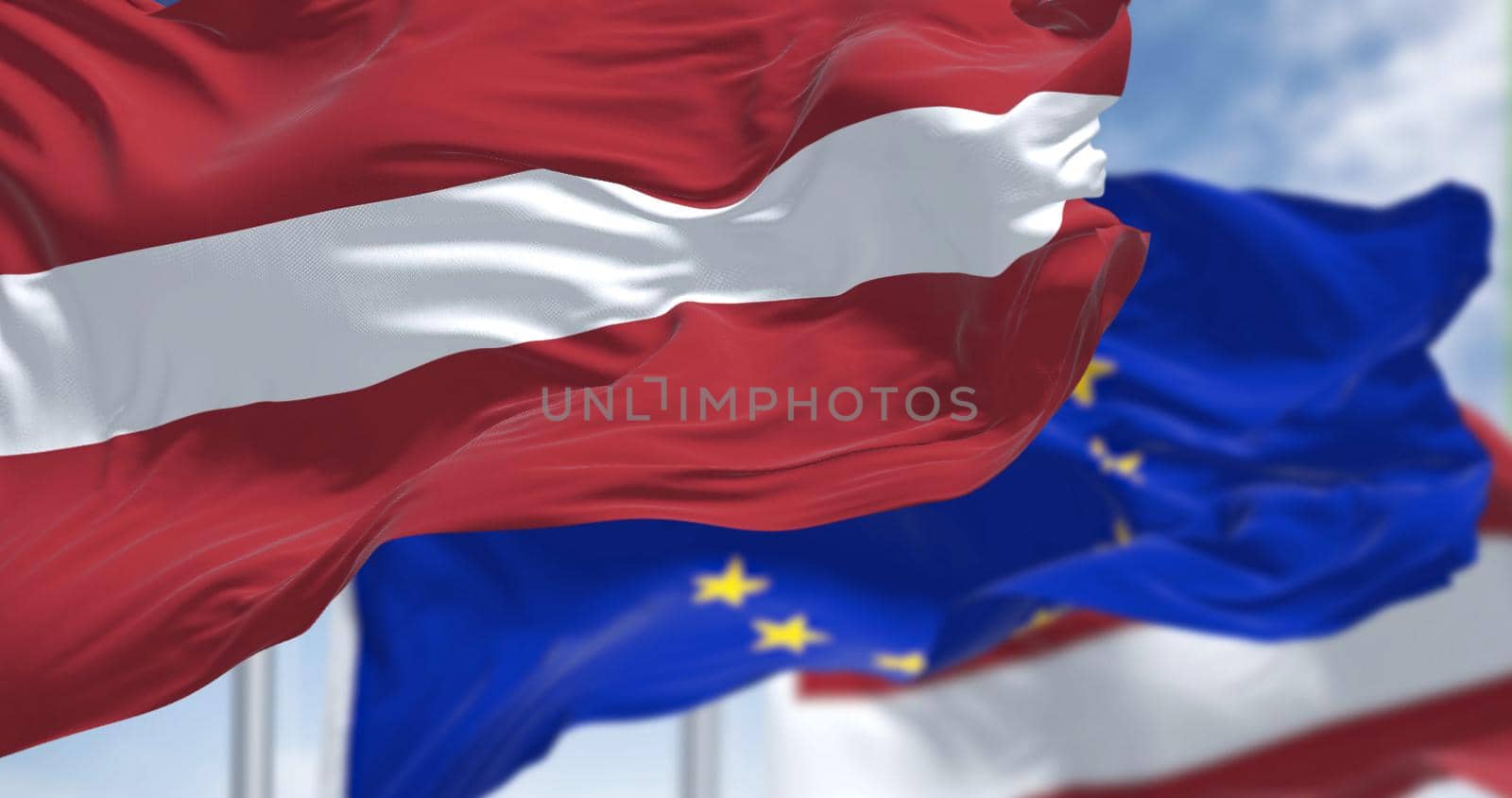 Detail of the national flag of Latvia waving in the wind with blurred european union flag in the background on a clear day. Democracy and politics. European country. Selective focus.