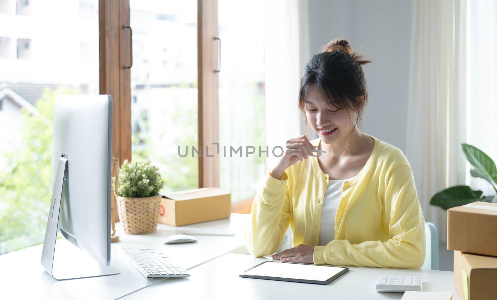 Portrait business Asian woman smile and use tablet checking information on parcel shipping box before send to customer. Entrepreneur small business working at home. SME business online marketing. by wichayada