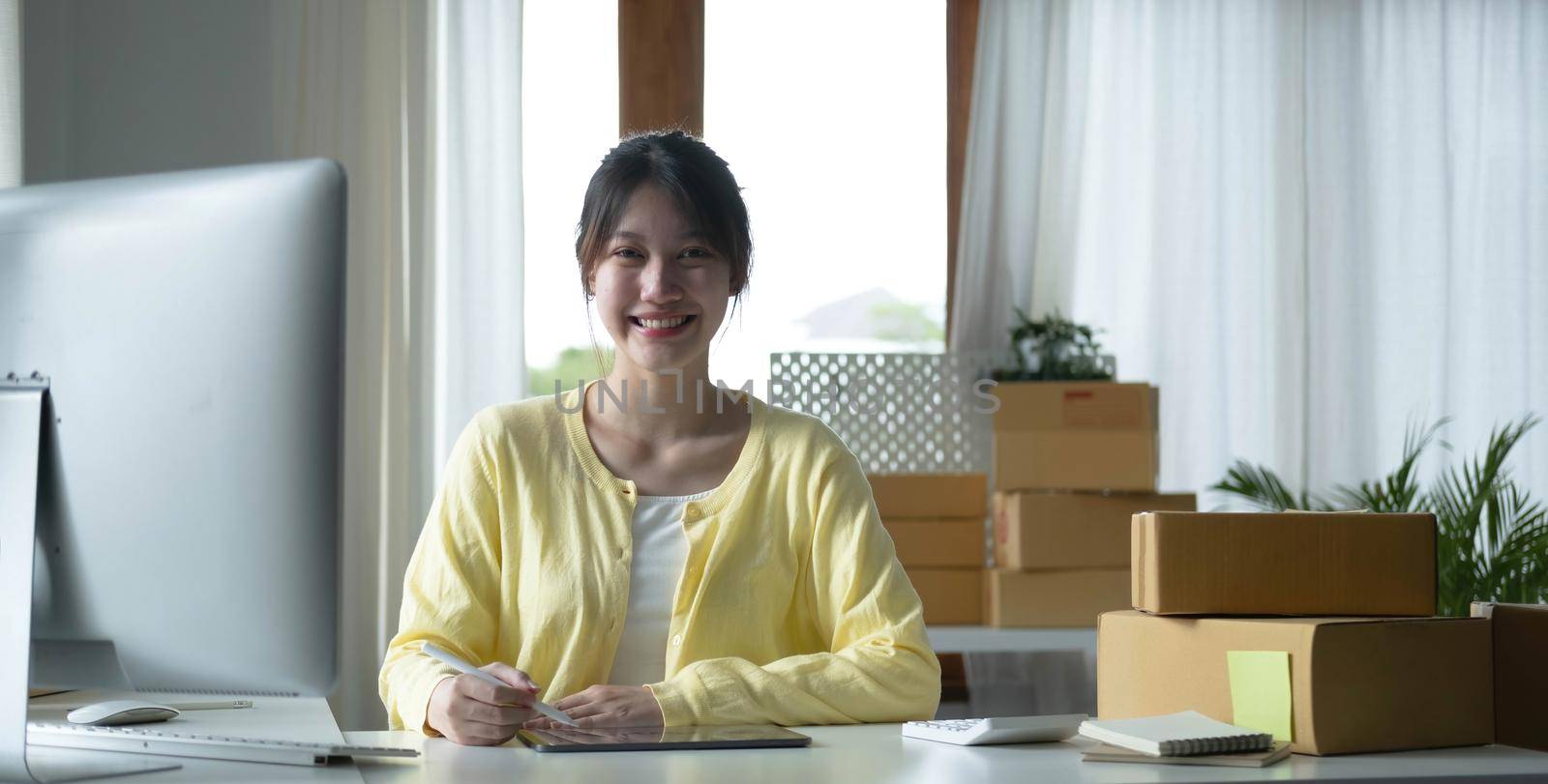 Portrait business Asian woman smile and use tablet checking information on parcel shipping box before send to customer. Entrepreneur small business working at home. SME business online marketing. by wichayada