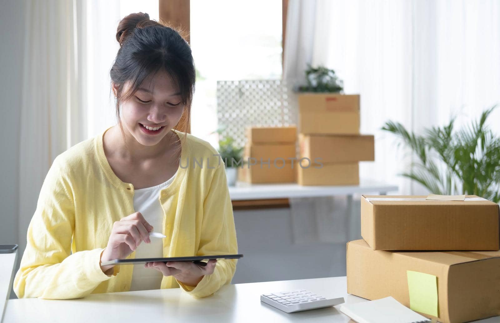 Portrait business Asian woman smile and use tablet checking information on parcel shipping box before send to customer. Entrepreneur small business working at home. SME business online marketing..