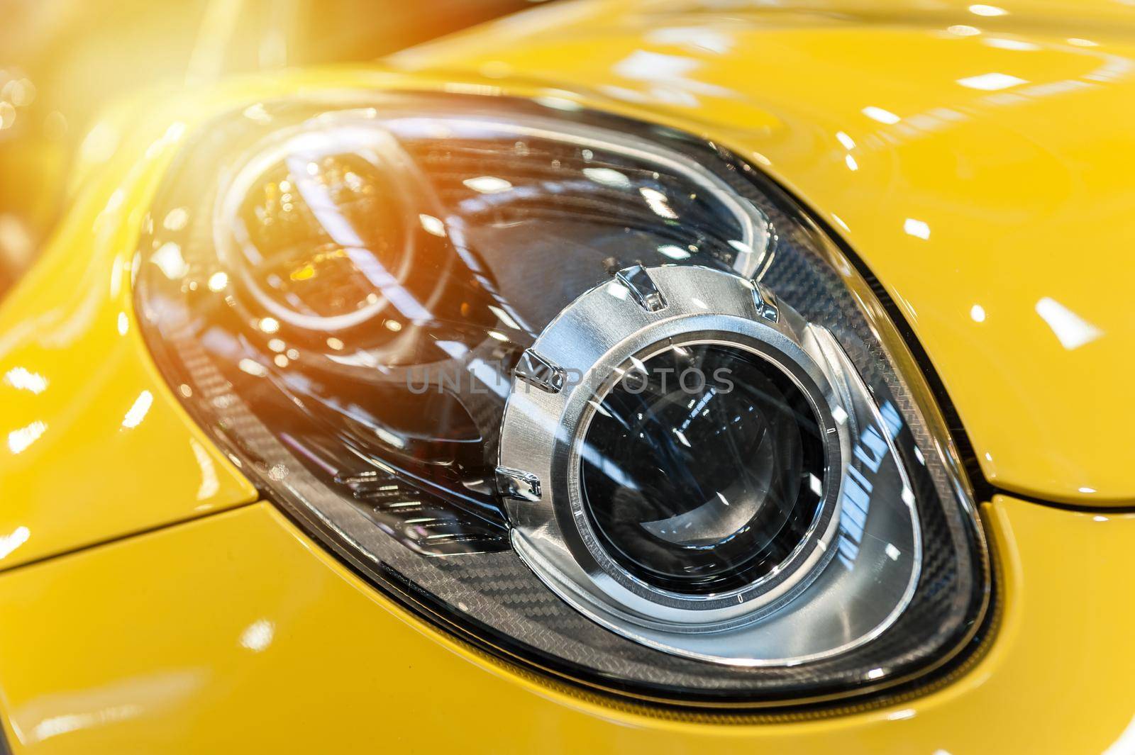 Closeup on an headlight of a yellow sport car in the sunlight