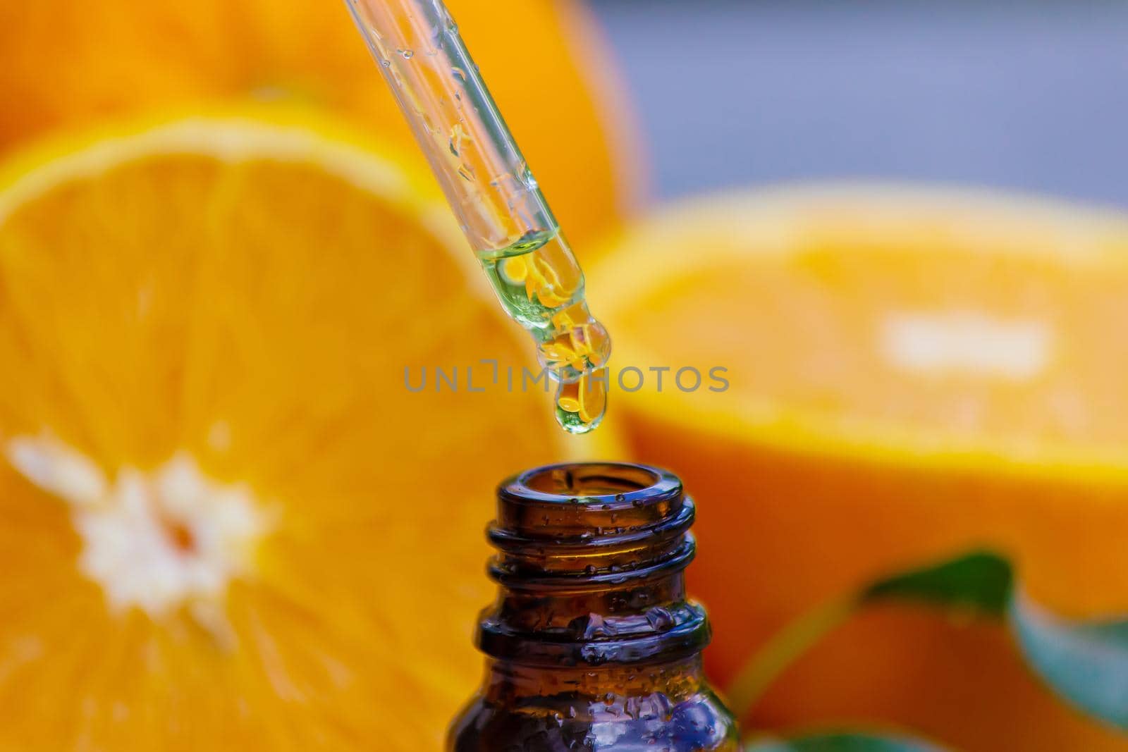 Essential orange oil in a bottle, fresh fruit pieces on the background. Natural flavors. Selective focus