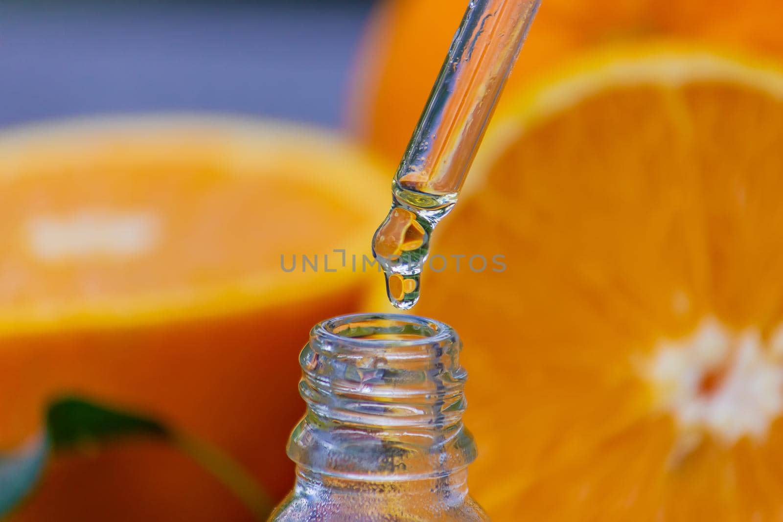 Essential orange oil in a bottle, fresh fruit pieces on the background. Natural flavors. Selective focus