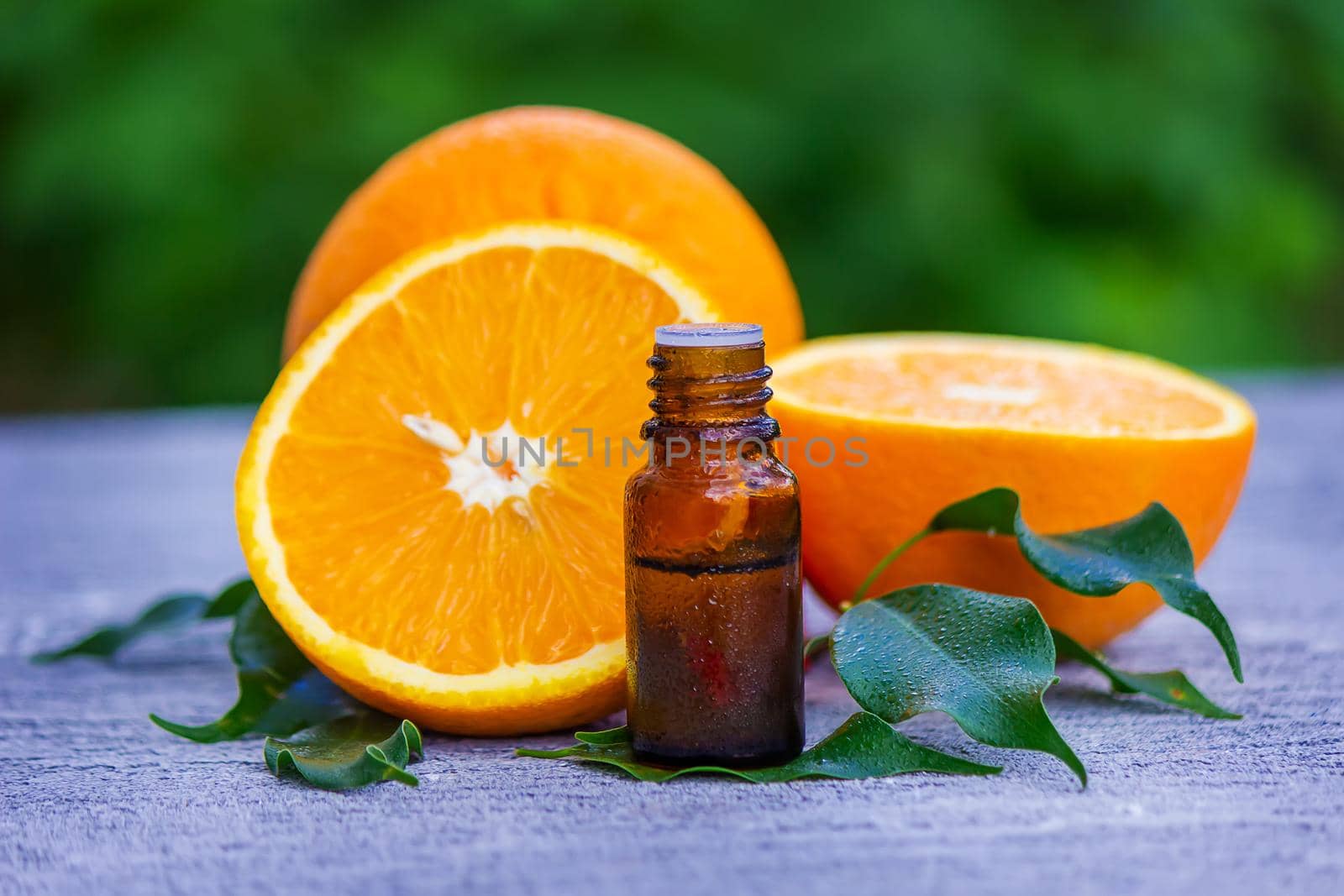 Essential orange oil in a bottle, fresh fruit pieces on the background. Natural flavors. Selective focus