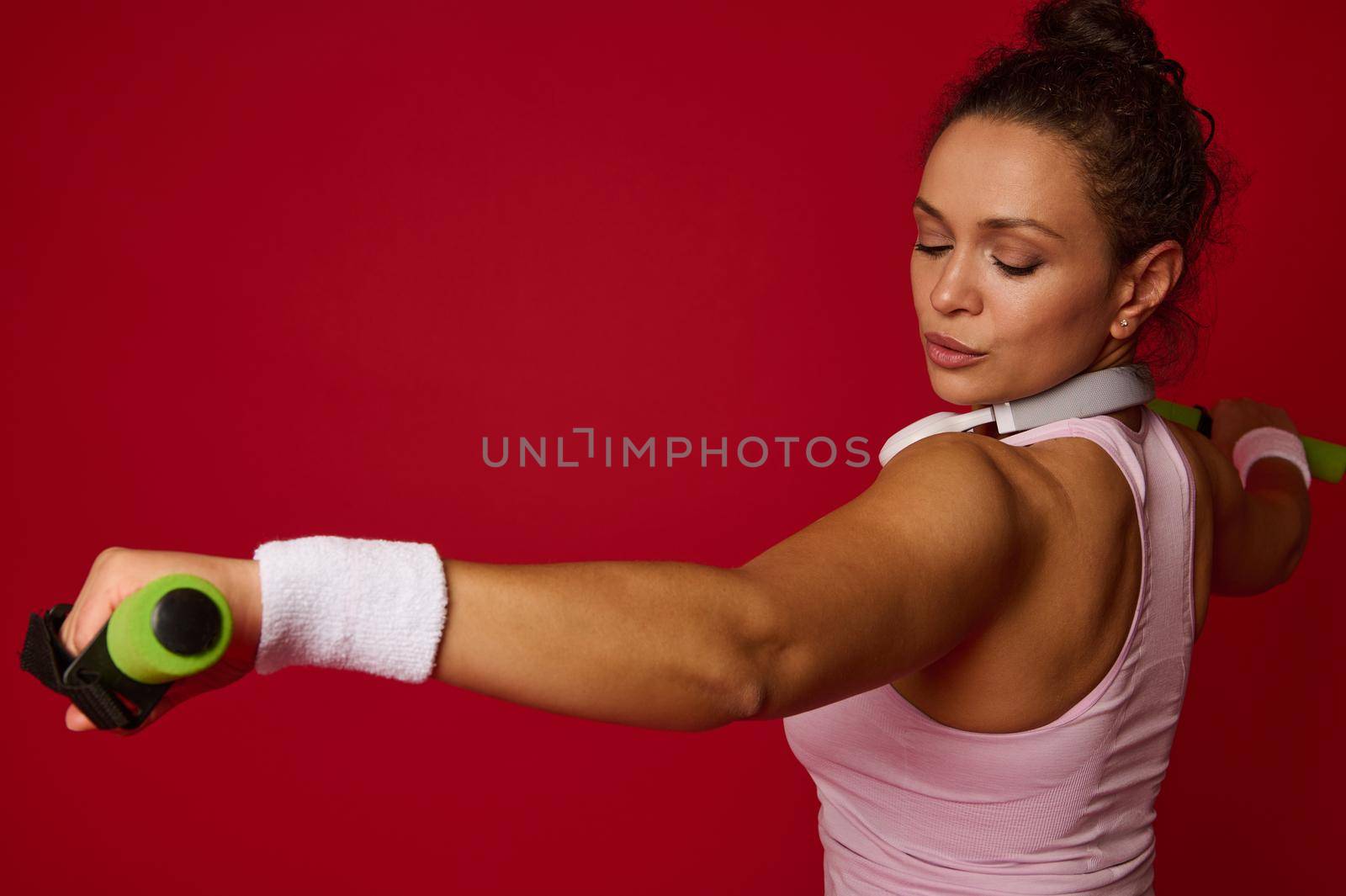 Close-up of young beautiful Hispanic fit sportswoman working out with dumbbells against red colored background with copy ad space. Sport, fitness, healthy and active lifestyle, weight loss concept