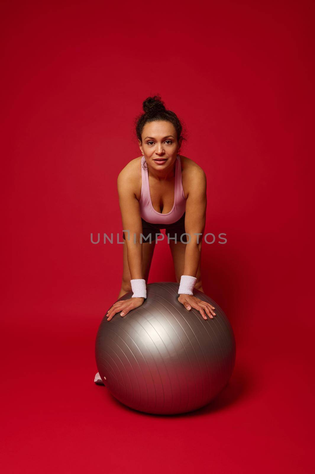 Portrait of a beautiful athlete woman with a fit ball isolated over red background with copy ad space by artgf