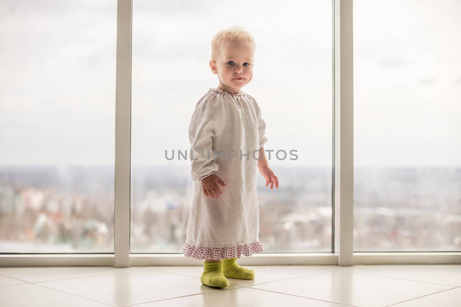 Charming baby girl with a blue eyes. Lovable infant at the big window