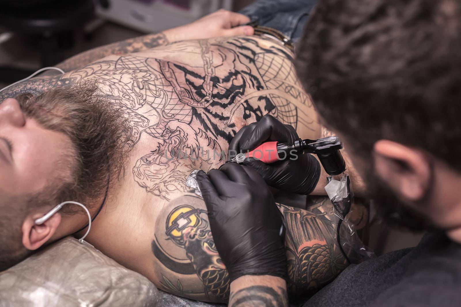 Master tattooist doing tattoo in tattoo parlor./Tattooer makes tattoo in tattoo studio.