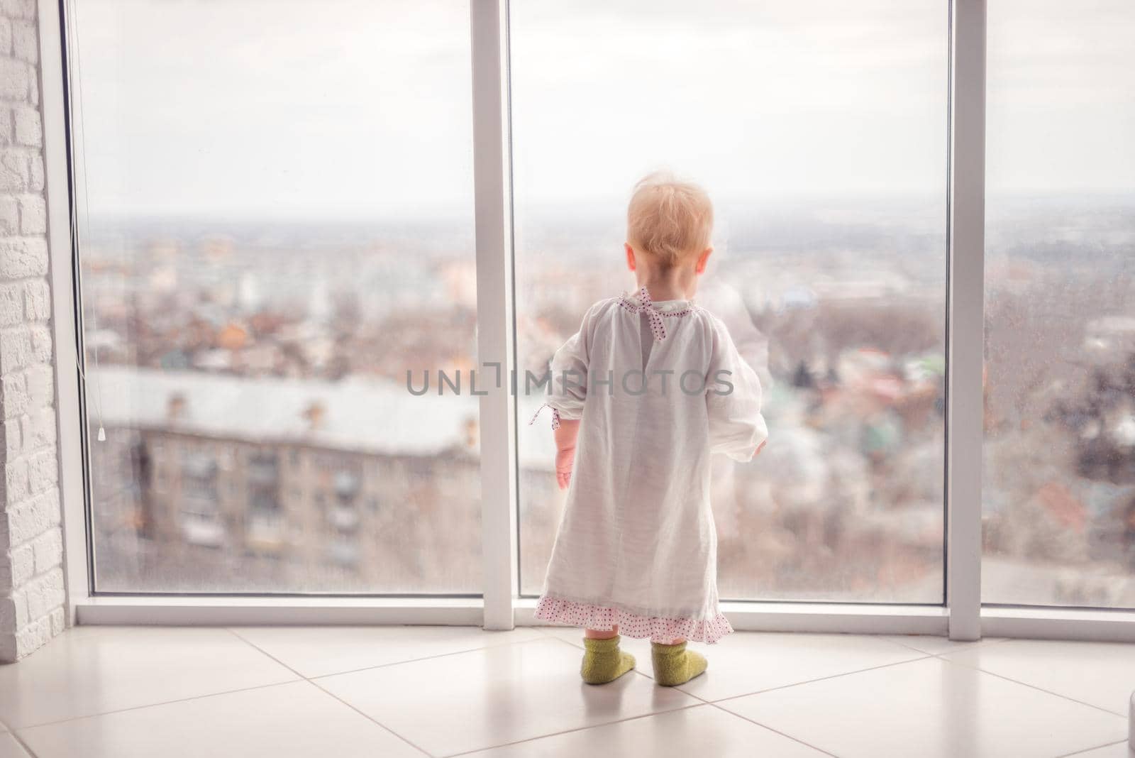 little girl in a cute dress looks out the window by Proff