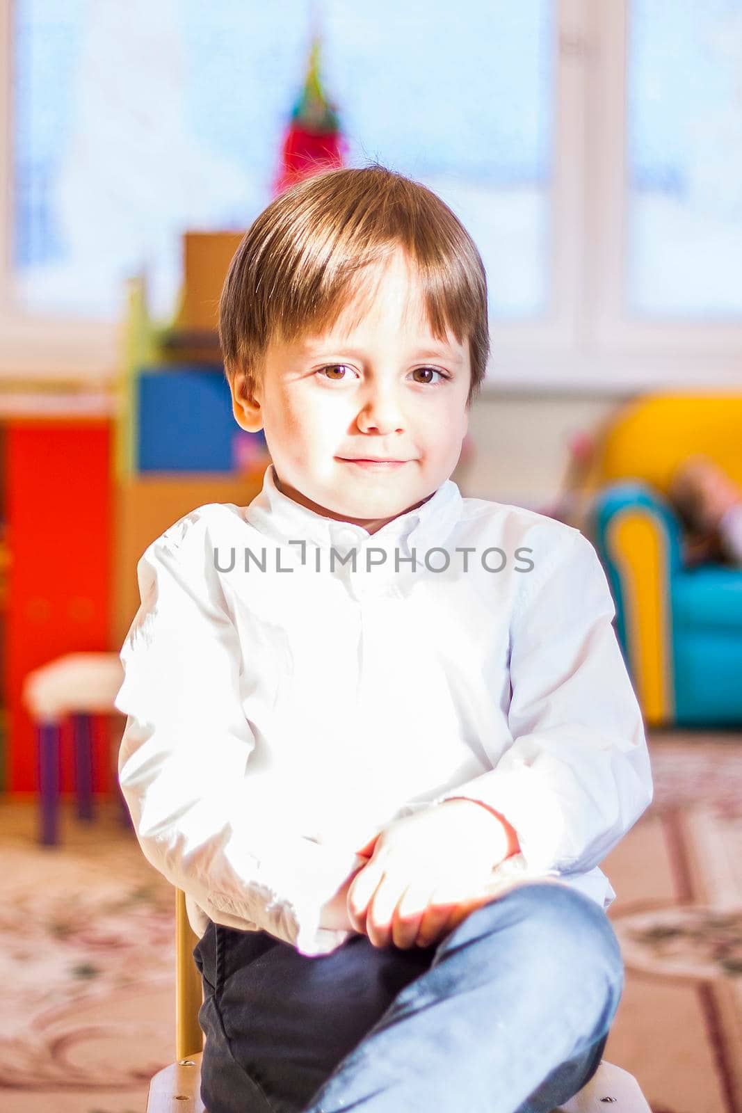 Elegantly dressed in a white shirt, a little boy is sitting in the classroom for lessons. portrait of a boy, blonde hair