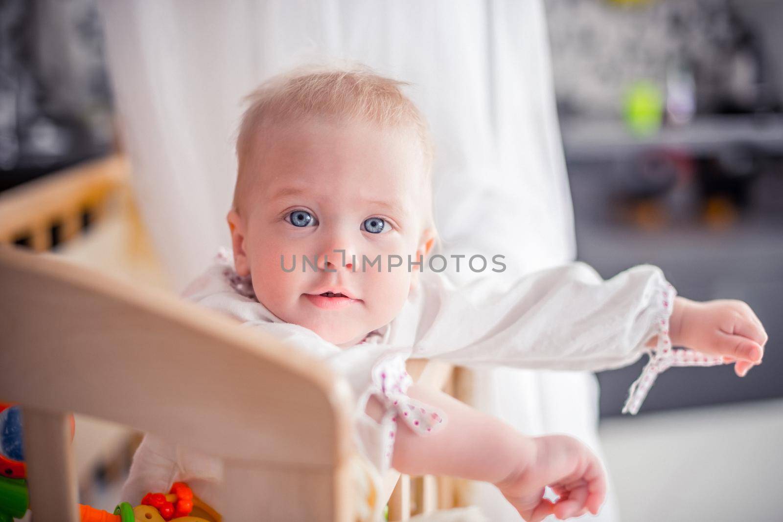 Baby with a cute happy face standing in a cot. by Proff