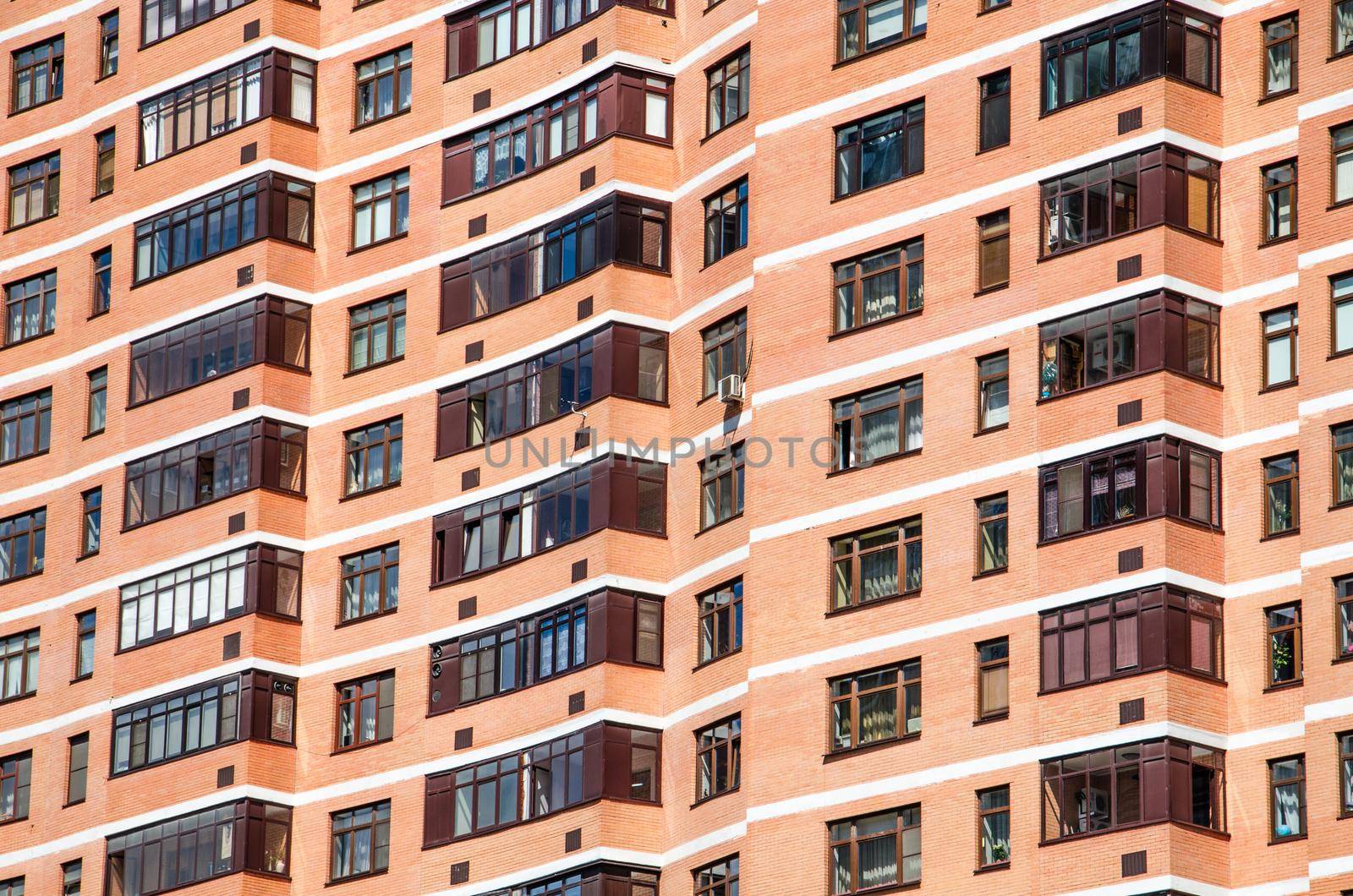 View of brick wall red contemporary apartment building with windows and balconies closeup.
