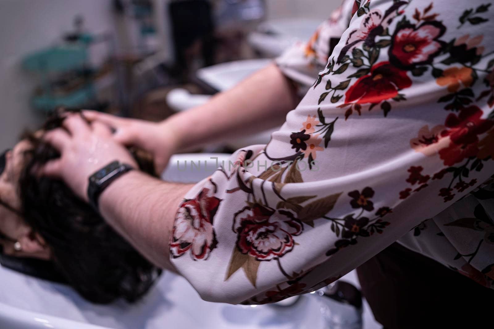 Senior woman enjoying head massage with closed eyes while professional hairdresser shampooing her hair. Hairstylist working with her female client