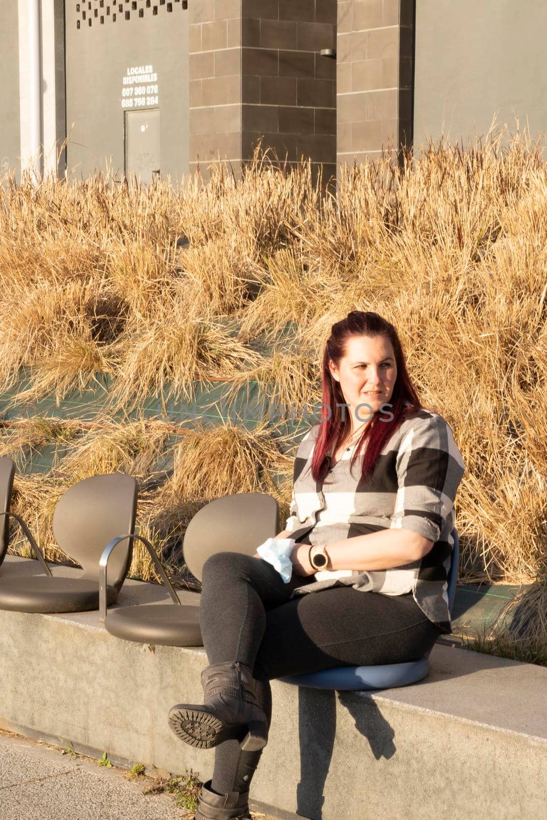 Young woman posing sitting on a bench, wearing a plaid shirt and reddish hair. casual look