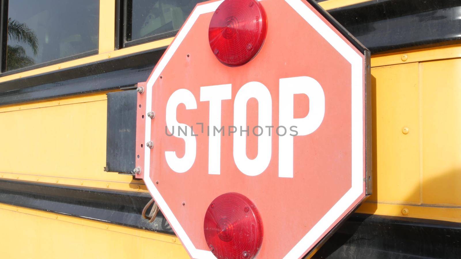 Red stop sign, yellow school bus in California, USA. Traffic warning on passenger schoolbus or shuttle in America. Public transportation safety on road. Caution or attention signage. Education concept