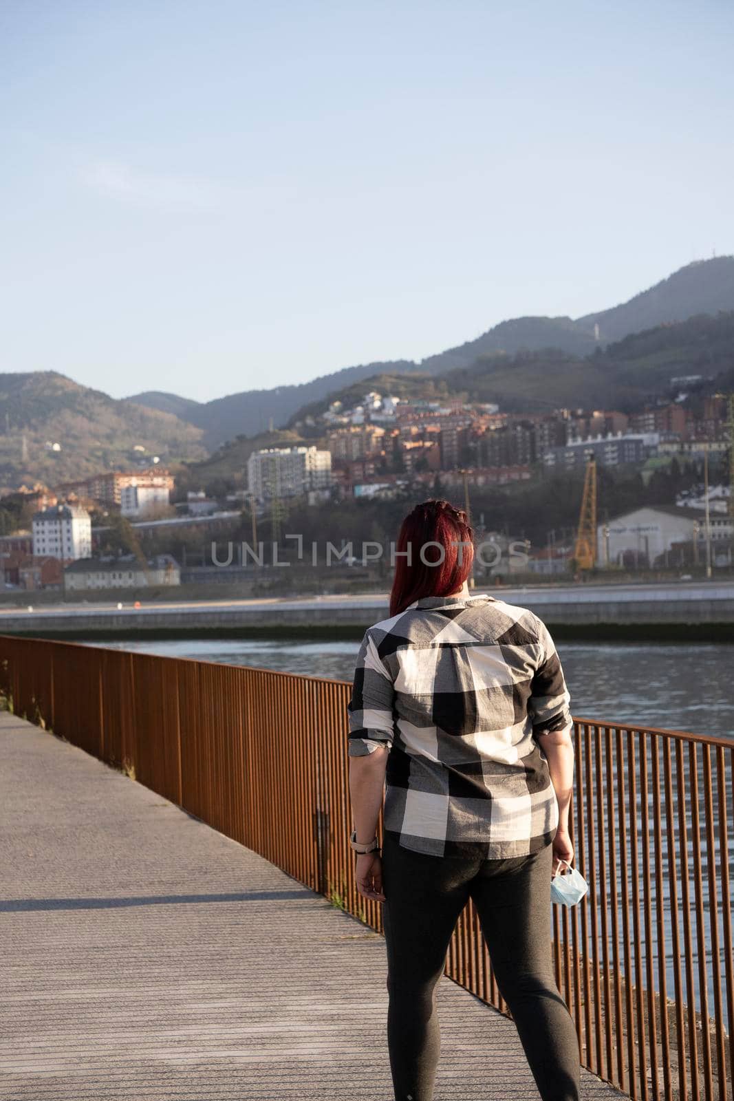 A young woman with long hair walking down the street with her hair blowing in the wind. She has her back to the camera.