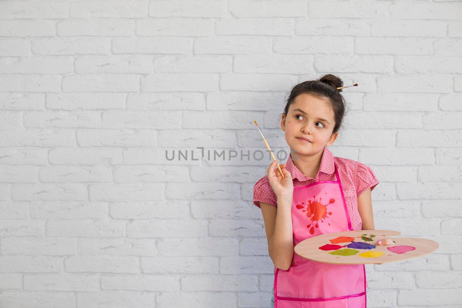portrait girl with paintbrush palette standing against white wall