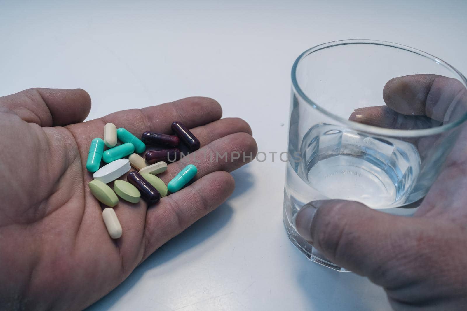 man's hand with pills in front of glass of water by barcielaphoto