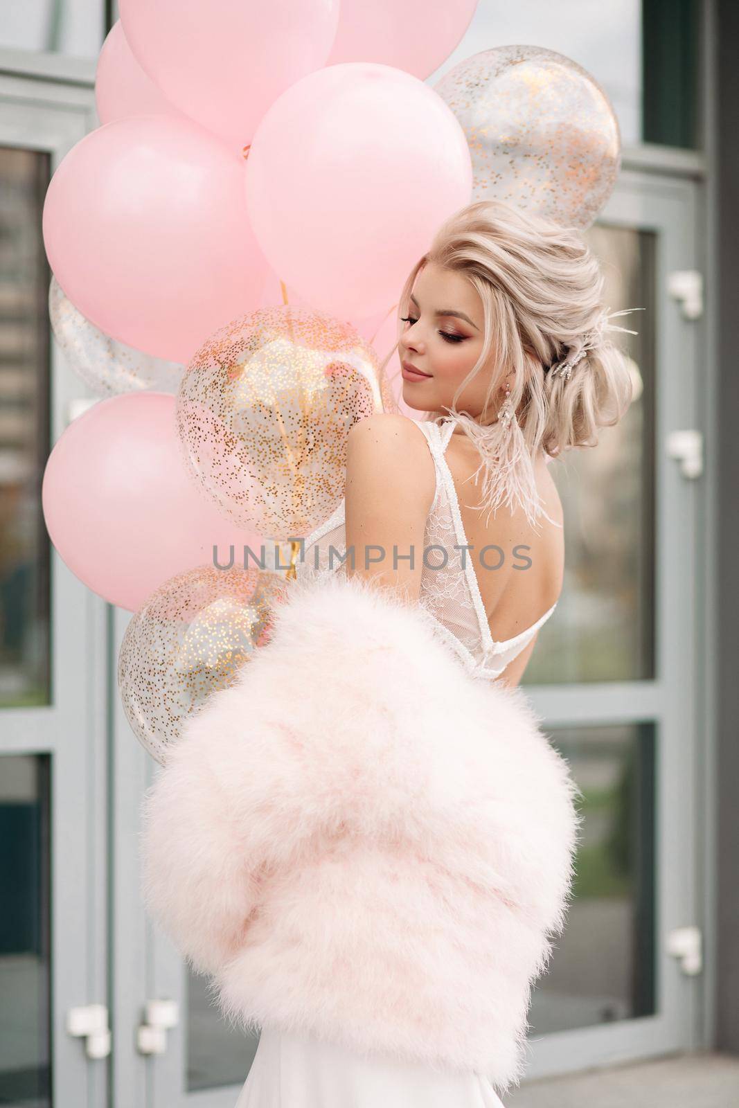 Stunning blonde woman in laced top or dress and pink fur coat with air balloons. by StudioLucky