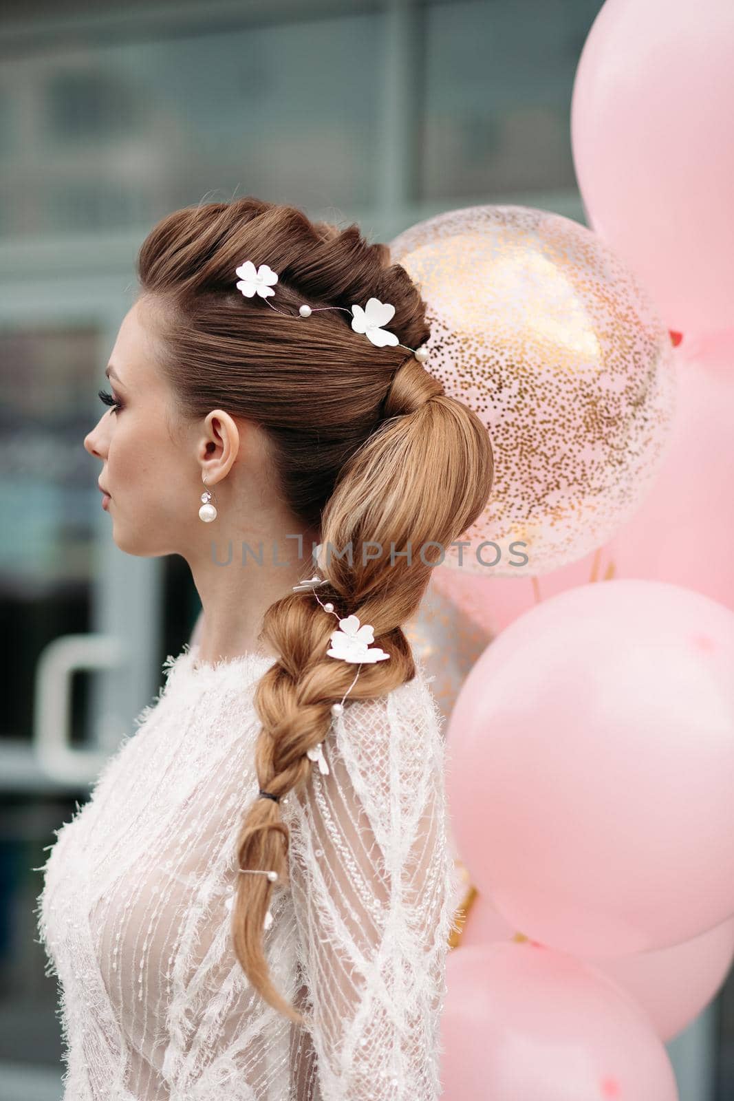 Back view of unrecognizable gorgeous brunette with beautiful hairdo and flowers in it posing in luxurious white dress with bunch on pink air balloons.