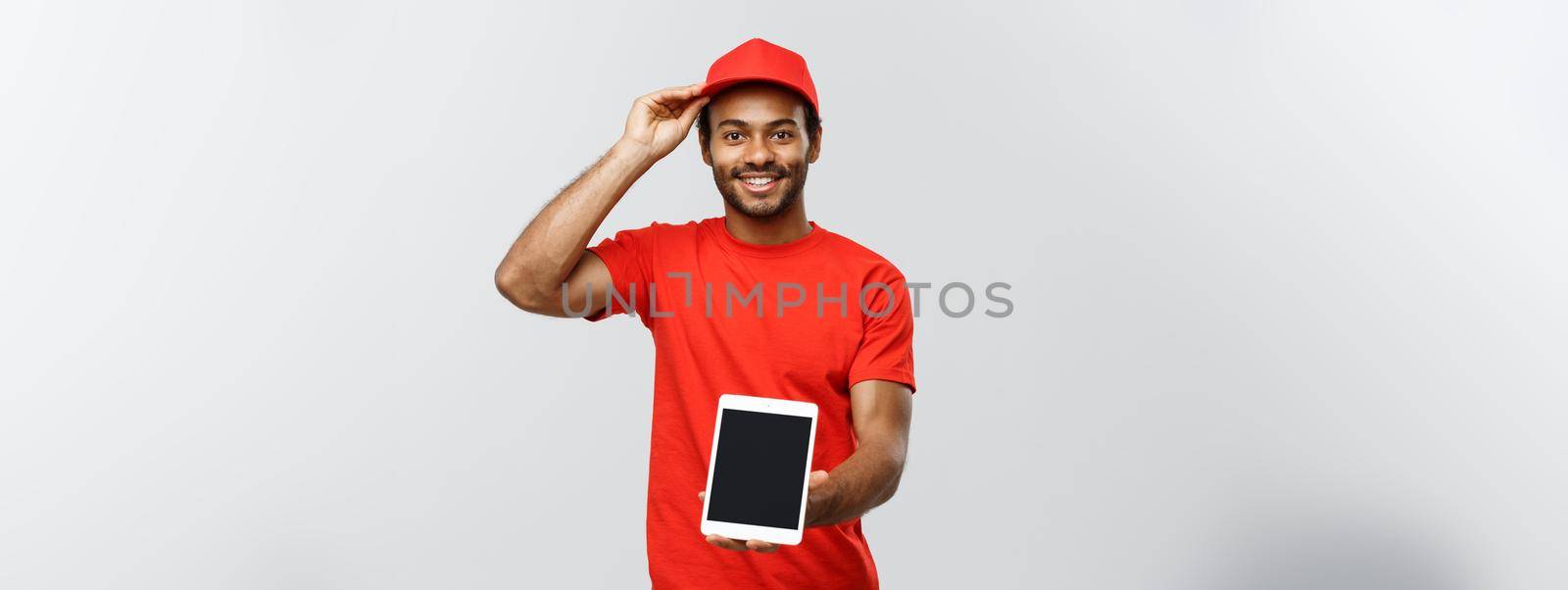 Delivery Concept - Portrait of Handsome African American delivery man or courier showing tablet on you to check the order. Isolated on Grey studio Background. Copy Space. by Benzoix