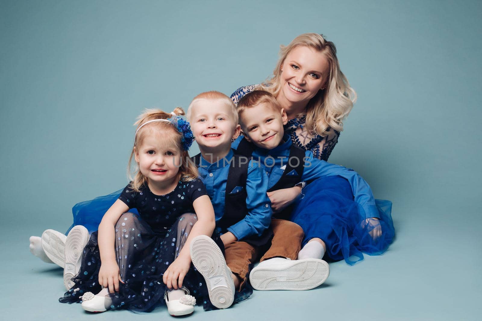 Studio portrait of happy smiling family of five posing and looking at camera together. Cheerful father embracing his children. Isolate on blue.