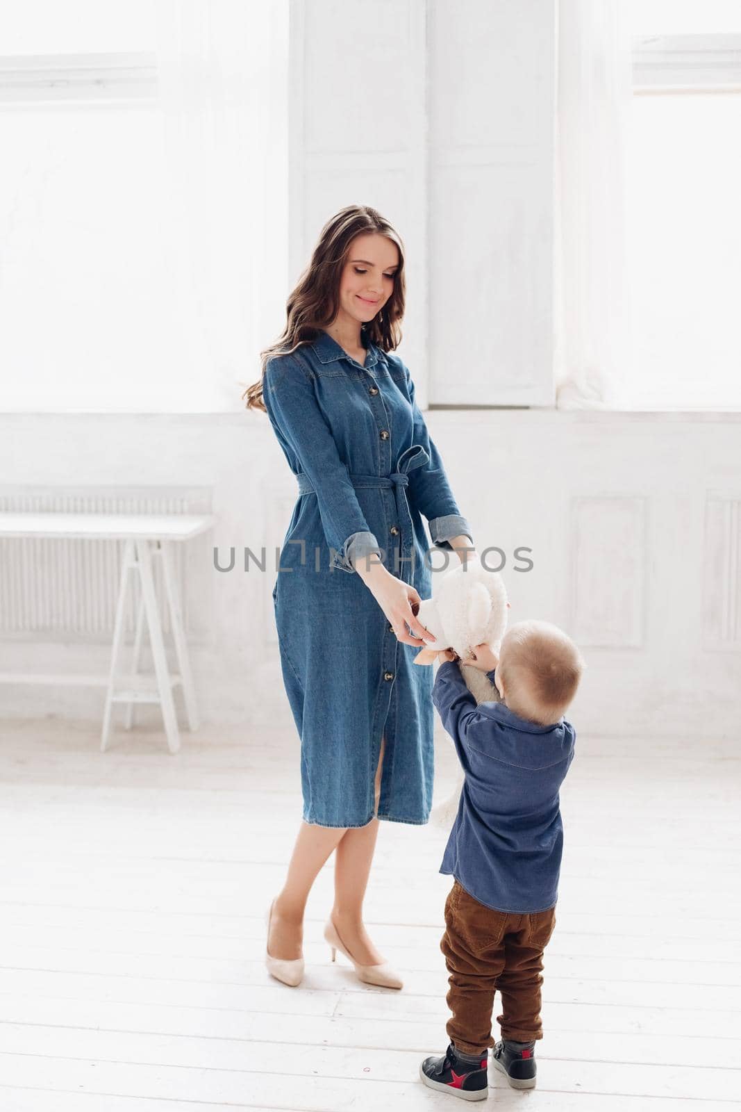 Portrait of gorgeous brunette young woman in casual denim dress embracing her lovely son in denim shirt on the bed. Family and motherhood concept.