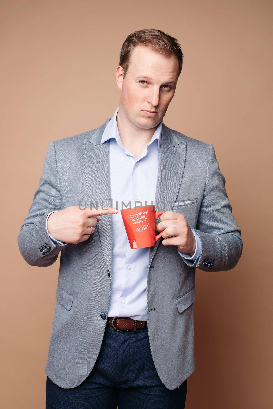 Studio portrait of determined successful businessman in suit and shirt holding red mug with positive slogan Everything is under control . He is smiling on isolate background.