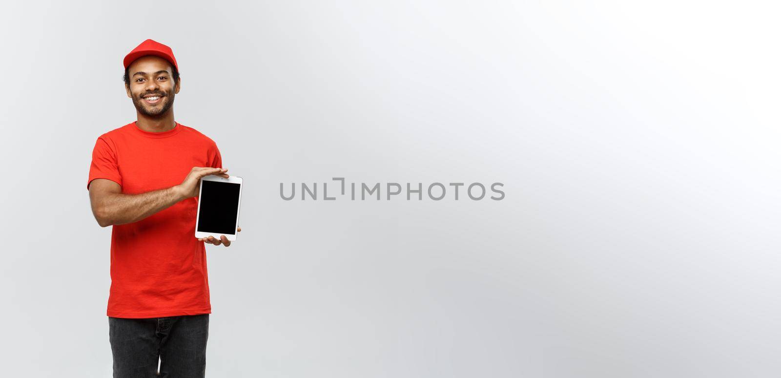 Delivery Concept - Portrait of Handsome African American delivery man or courier showing tablet on you to check the order. Isolated on Grey studio Background. Copy Space. by Benzoix