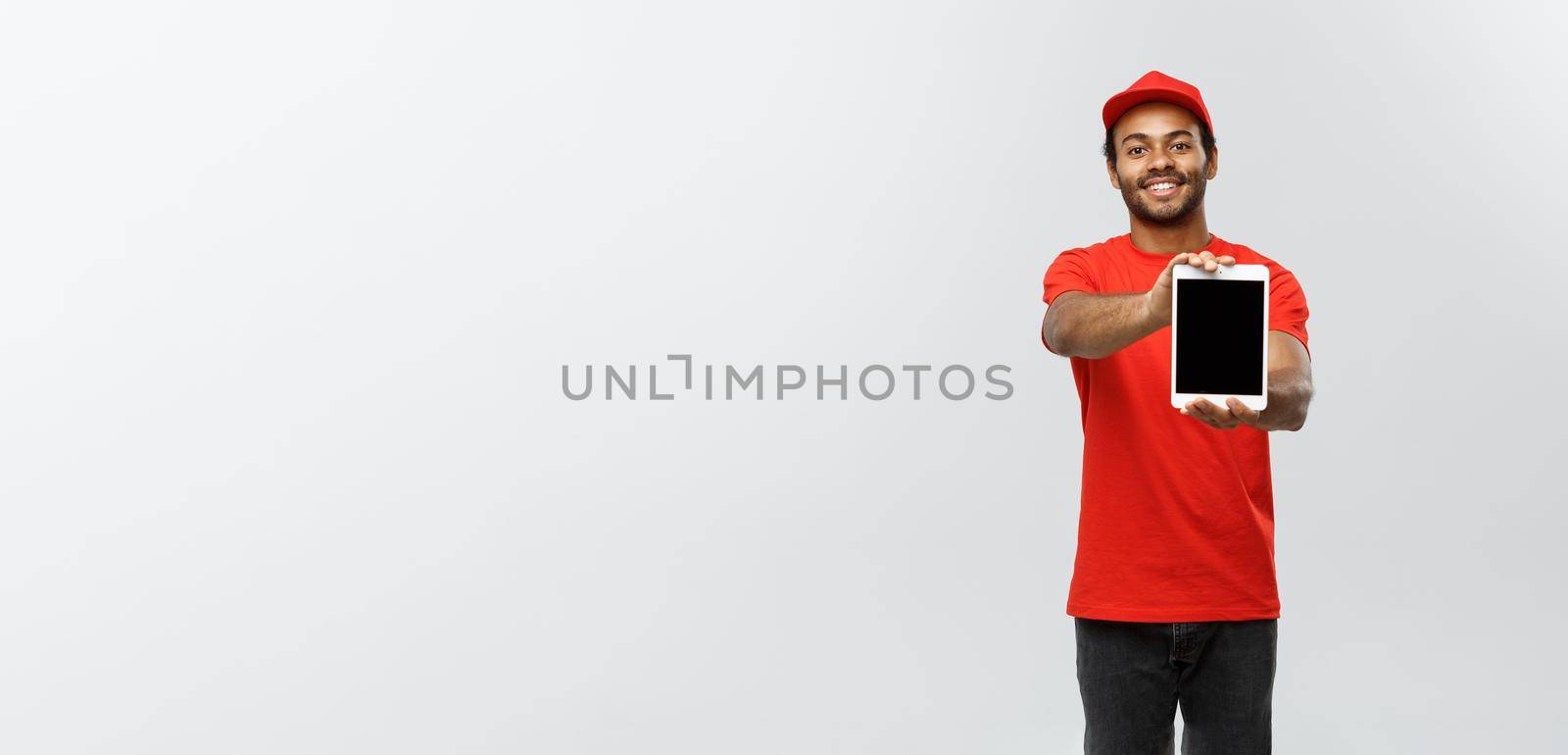 Delivery Concept - Portrait of Handsome African American delivery man or courier showing tablet on you to check the order. Isolated on Grey studio Background. Copy Space