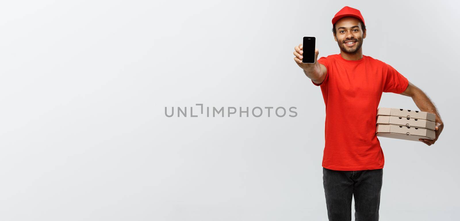 Delivery Concept - Portrait of Handsome African American delivery man or courier with pizza box showing mobile phone on you to check the order. Isolated on Grey studio Background. Copy Space. by Benzoix