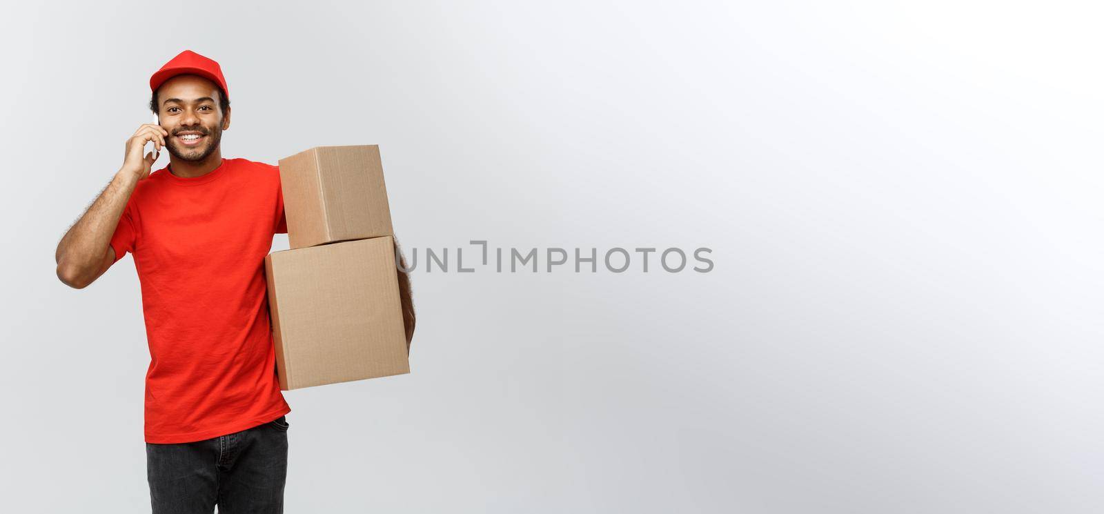 Delivery Concept - Portrait of Handsome African American delivery man or courier with box calling phone to customer. Isolated on Grey studio Background. Copy Space